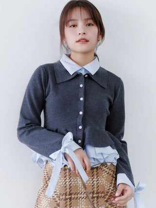 A young woman modeling a dark gray cardigan layered over a light blue collared shirt, paired with a brown and beige plaid skirt, against a plain white background.