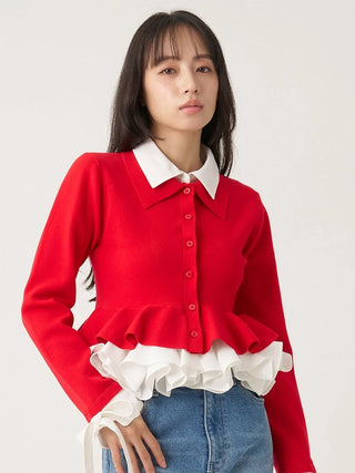 A woman wearing a bright red long-sleeve button-front top with a white pointed collar and white ruffled trim at the waist, paired with blue jeans, against a plain light background.