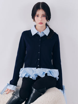 A woman models a dark navy long-sleeve button-front cardigan layered over a light blue collared shirt, with a matching light blue ruffled hem detail and light blue tie cuffs, paired with black leggings and black knee-high boots against a plain light gray background.