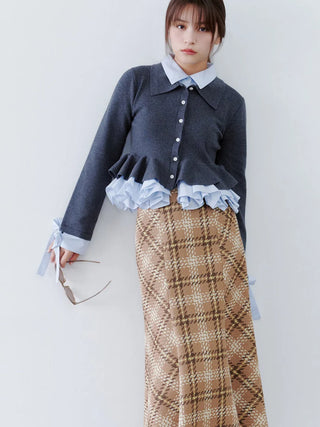 A model wearing a dark gray cardigan with light blue ruffle details, a light blue collared shirt underneath, and a brown plaid maxi skirt, holding a pair of sunglasses against a plain white background.