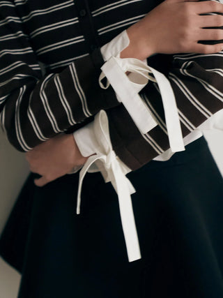 Close-up of a person wearing a black and white striped long-sleeve top with wide white ties at the cuffs, paired with a dark skirt.