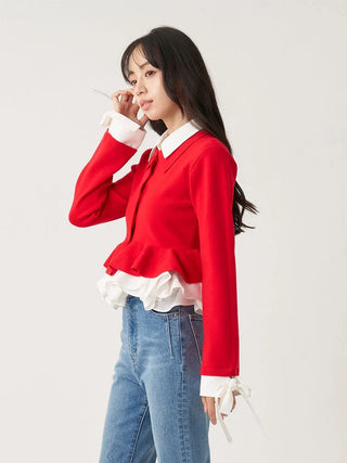 A woman modeling a bright red long-sleeve cardigan with a white ruffled collar and hem, paired with blue jeans, against a plain light gray studio background.