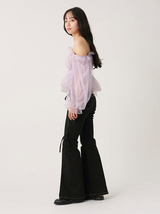 A woman modeling a light pink off-the-shoulder sheer puff-sleeve blouse paired with black wide-leg pants, standing against a plain light gray studio background.