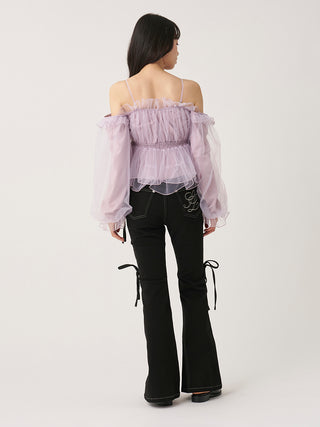 A model shown from the back wearing a light purple off-the-shoulder ruffled top with long sheer puff sleeves and black flared jeans with side tie details, against a plain light gray studio background.
